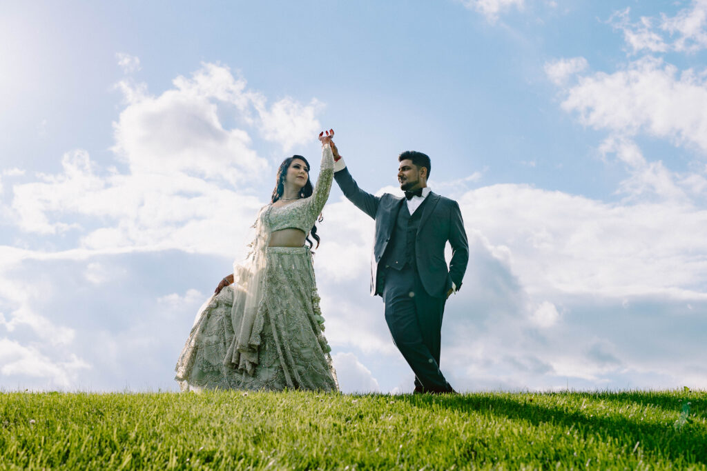 Traditional Indian bride and groom portraits. They are on green grass with blue sky and a few white fluffy clouds
