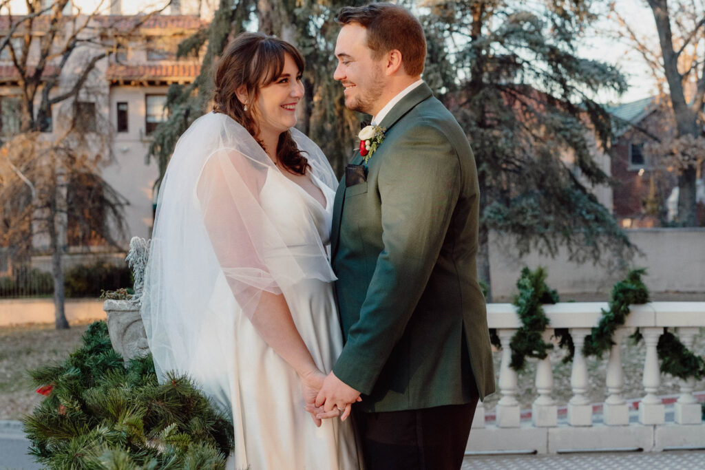 Bride and groom leaning on a railing. Groom is in a green jacket and bride has on a veil