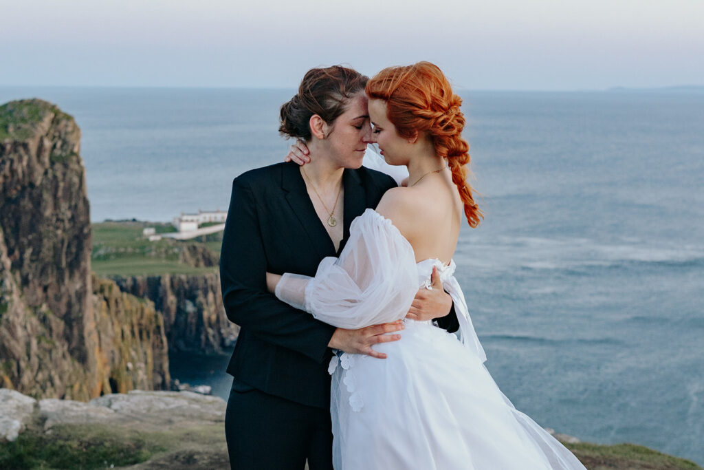 two brides looking at eachother with the neist point lighthouse behind them
