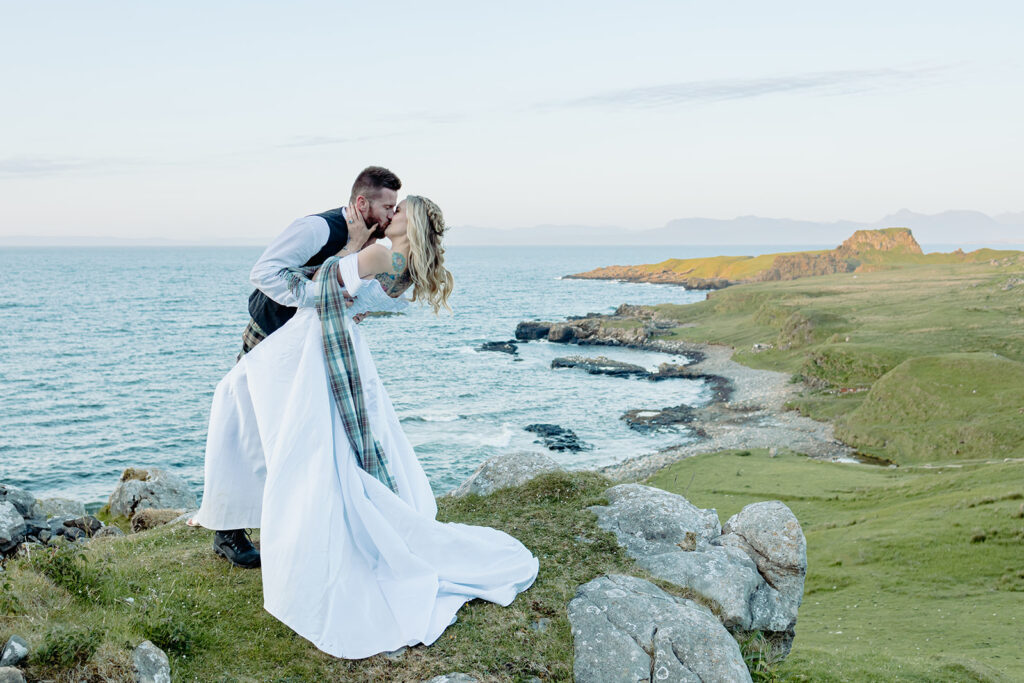 Bride and groom in traditional Scottish attire kissing at Brother's Point in Scottland UK