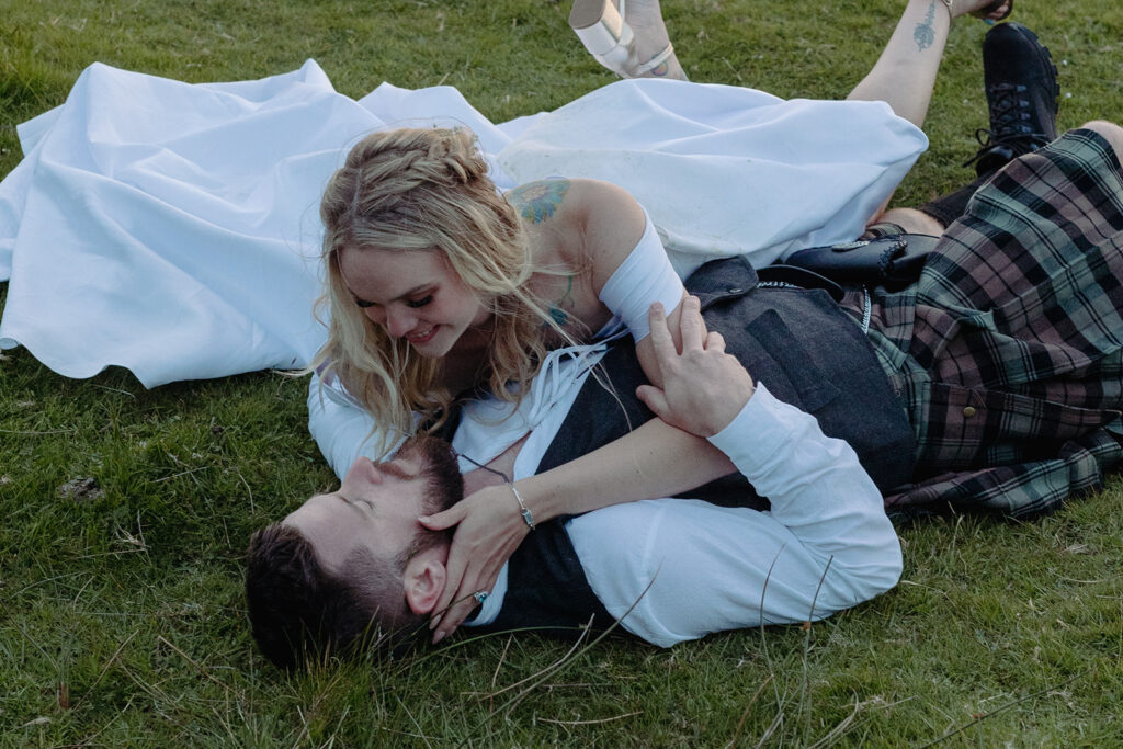 bride and groom rolling around in the grass. groom is wearing traditional Scottish attire.