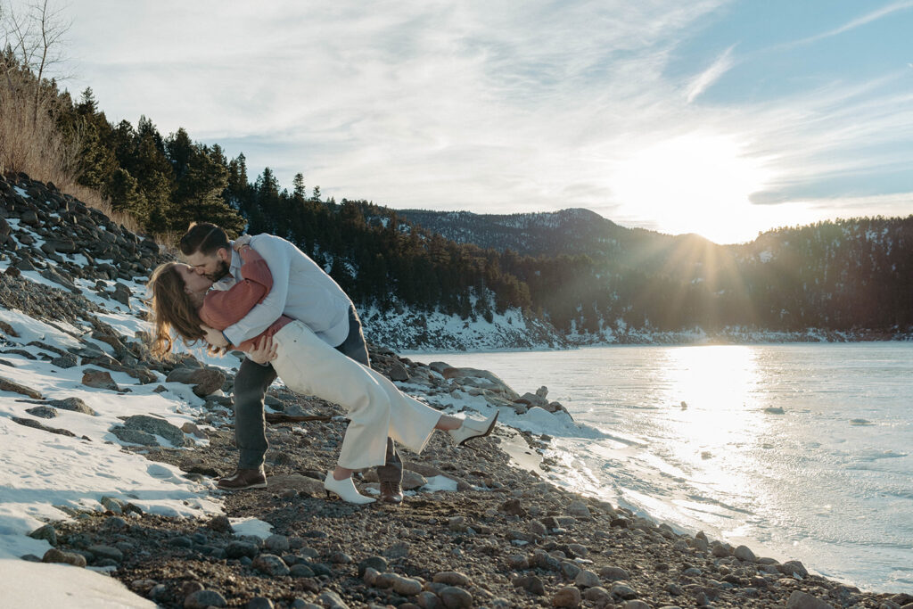 An adventurous couple kissing by a frozen lake