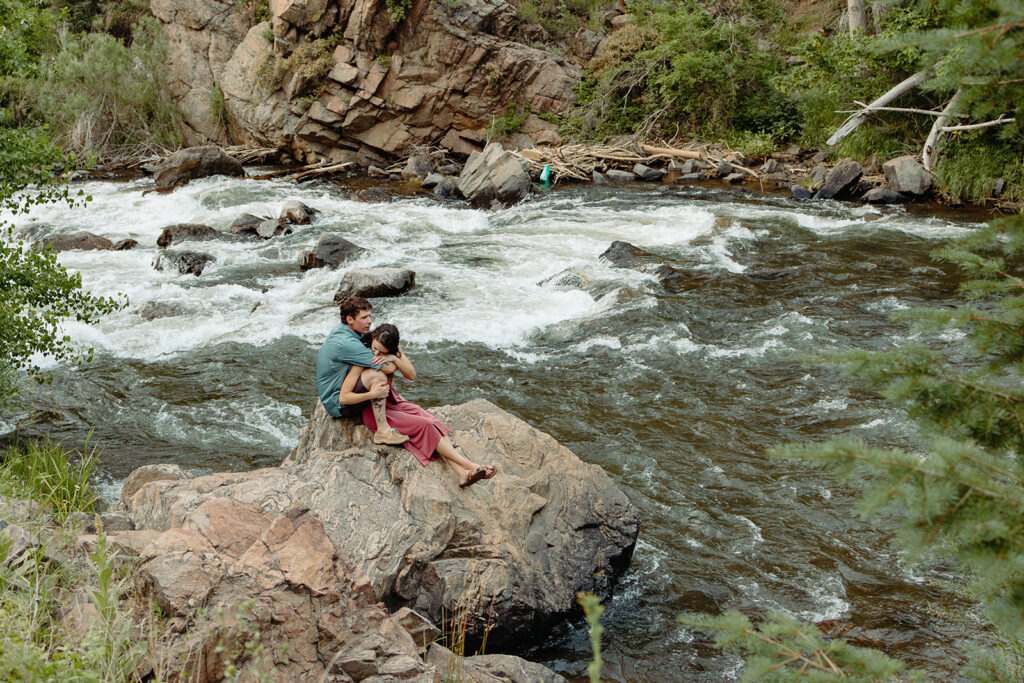 Two adventurous people sitting on a rock by some rapids